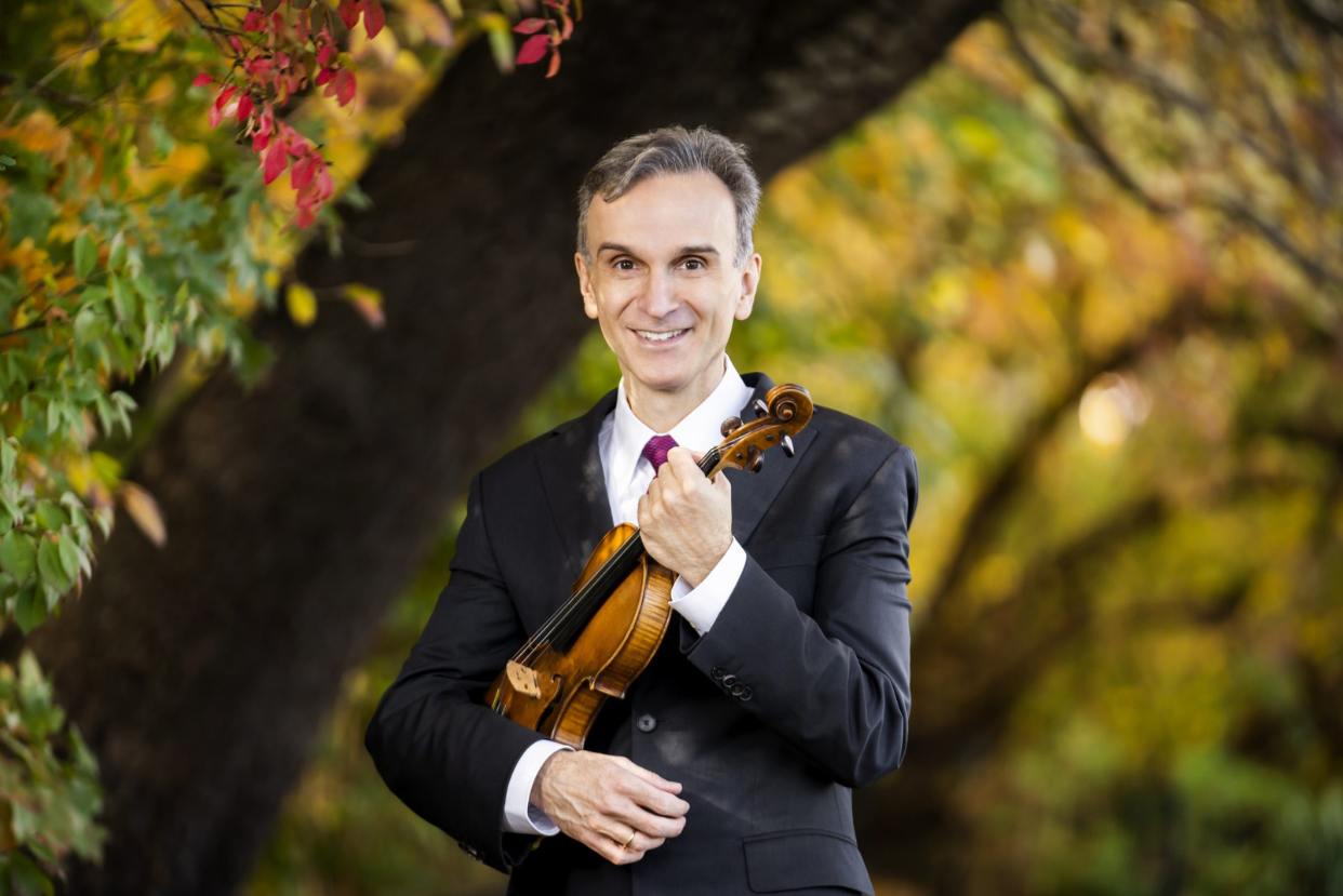 A man in a black suit holding a violin in an autumn forest